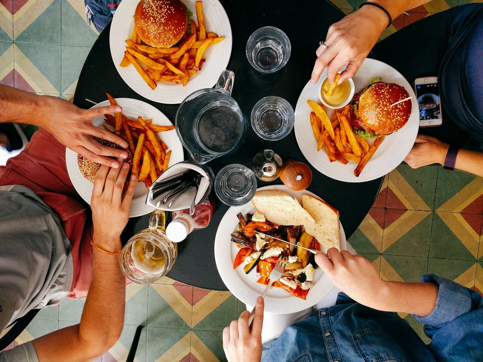 Comensales en la mesa de un restaurante compartiendo hamburguesas, con el celular a un costado